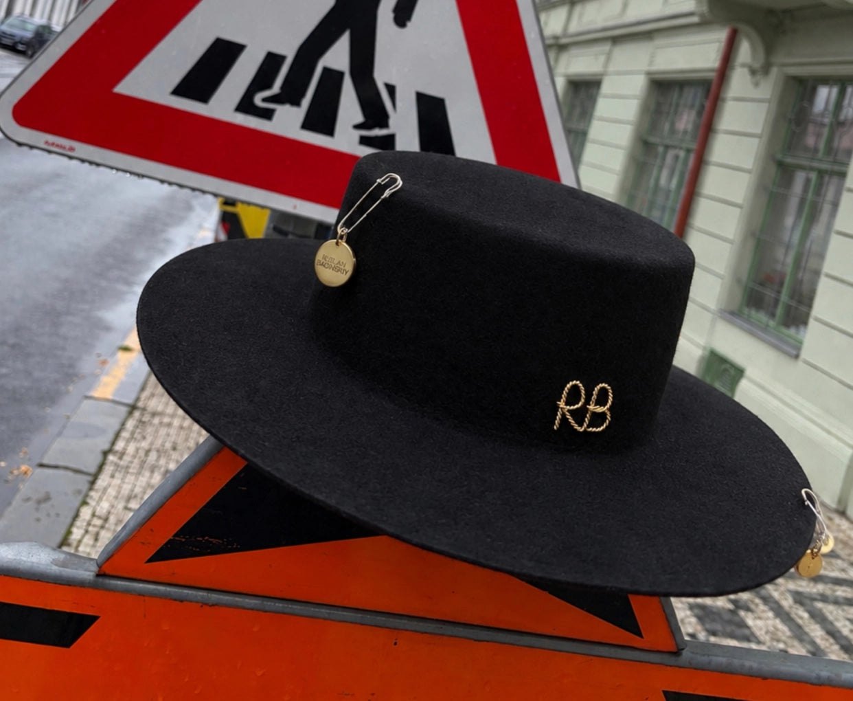 Black wide brim hat with gold RB pin resting on a street sign